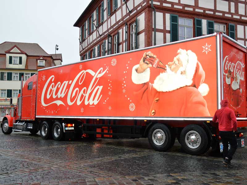 Ein riesiger LKW mit Coca-Cola-Schriftzug und Weihnachtsmann, der eine Cola trinkt, steht auf dem Marktplatz vor dem Rathaus