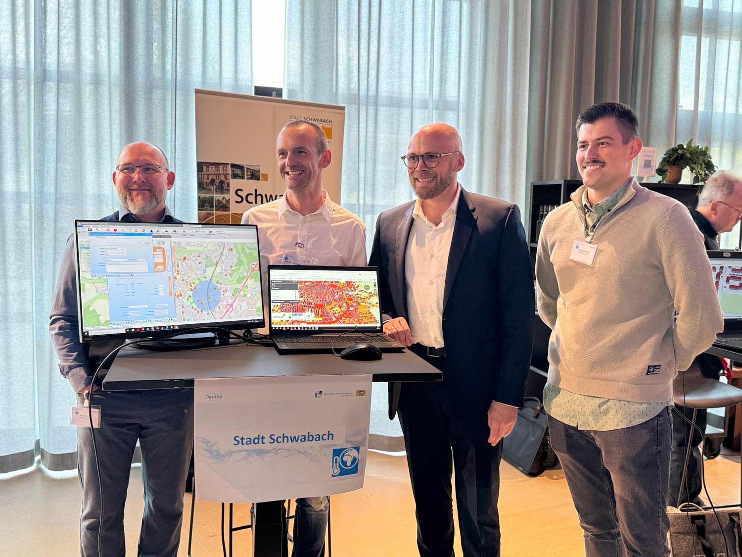 Vier Männer stehen hinter zwei Monitoren auf einem Flatscreen und einem Laptop auf denen Karten von der Stadt Schwabach zu sehen sind.