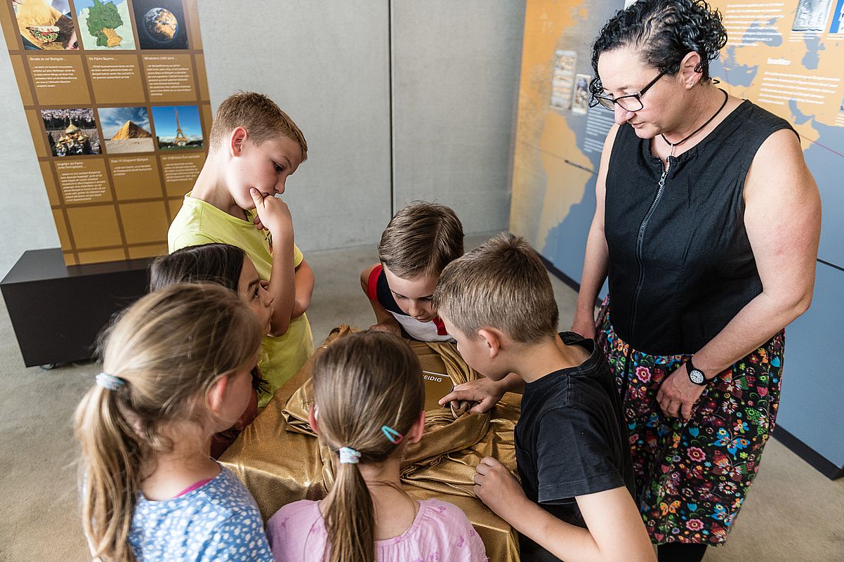 Kinder bei einer Führung beugen sich über ein kleines Gold-Nugget in der Goldabteilung des Schwabacher Stadtmuseums