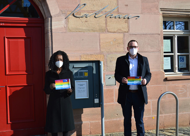 Sandra Niyonteze und Peter Reiß stehen vor dem Rathaus mit einer Botschaft für Toleranz und gegen Rassismus