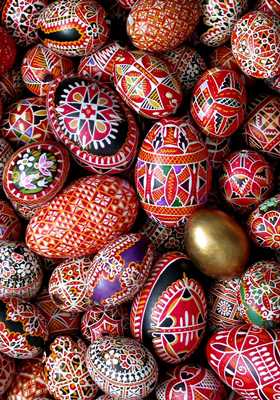 Rot, dunkelblau und weitere bemalte Ostereier liegen auf einem Haufen. Dazwischen ein vergoldetes Ei.