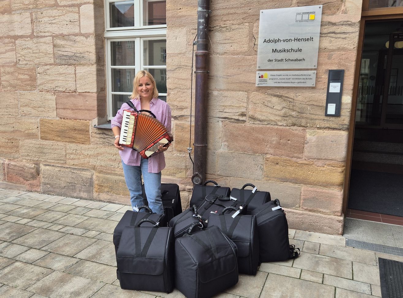 Neue Akkordeonlehrerin steht mit 11 neuen Akkordeons vor Musikschule