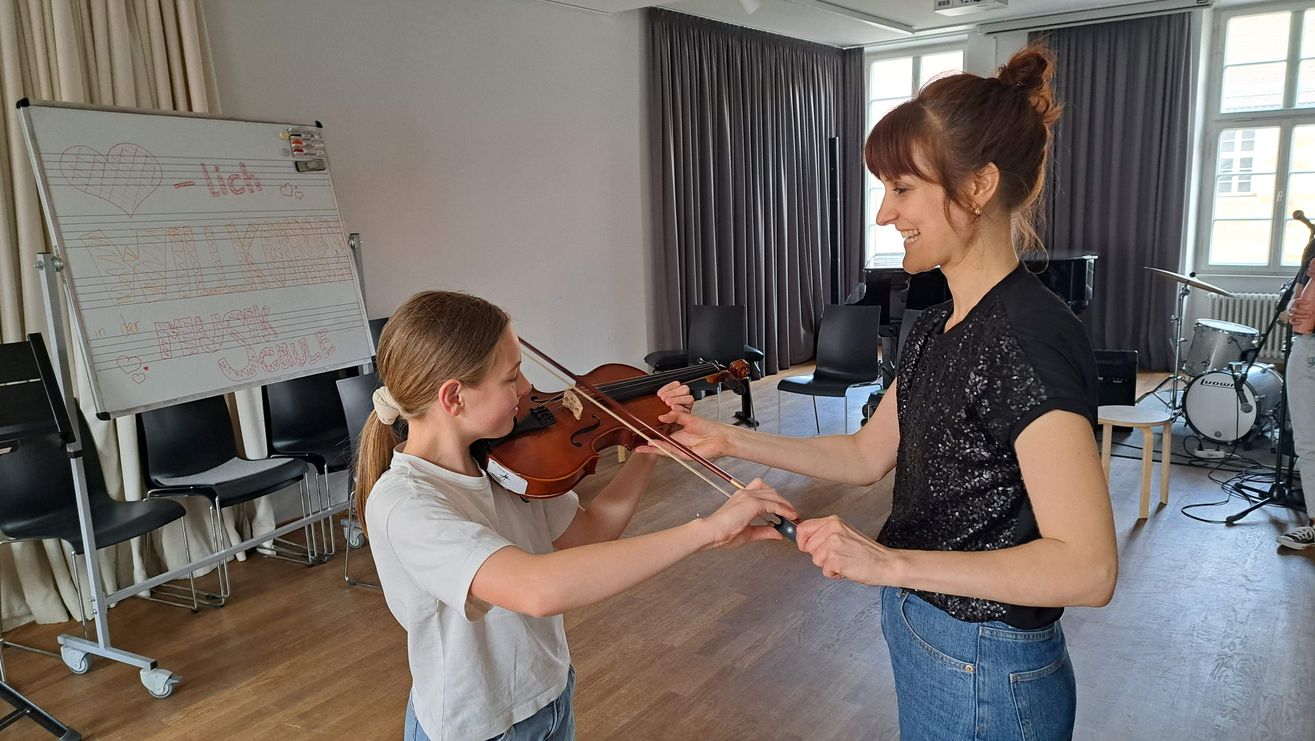 Kind probiert die Violine in Anwesenheit einer Lehrerin