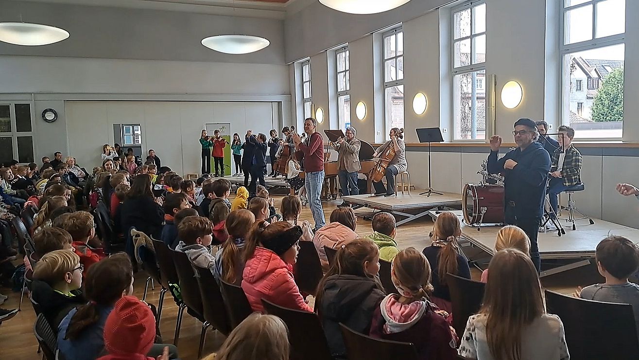 Schüler hören Lehrern und Musikschülerinnen zu