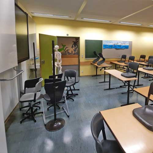 Klassenzimmer mit hochgestellten Stühlen und einem Skelett sowie Whiteboard