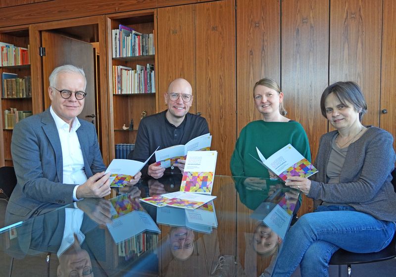 Vier Menschen sitzen an einem Tisch und schauen sich die neue Broschüre an.