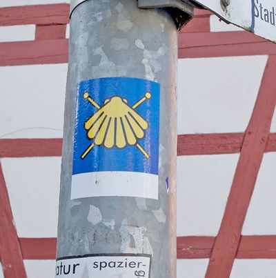 Ein Aufkleber mit einer gelben Muschel auf blauem Grund klebt an einem Lichtmasten