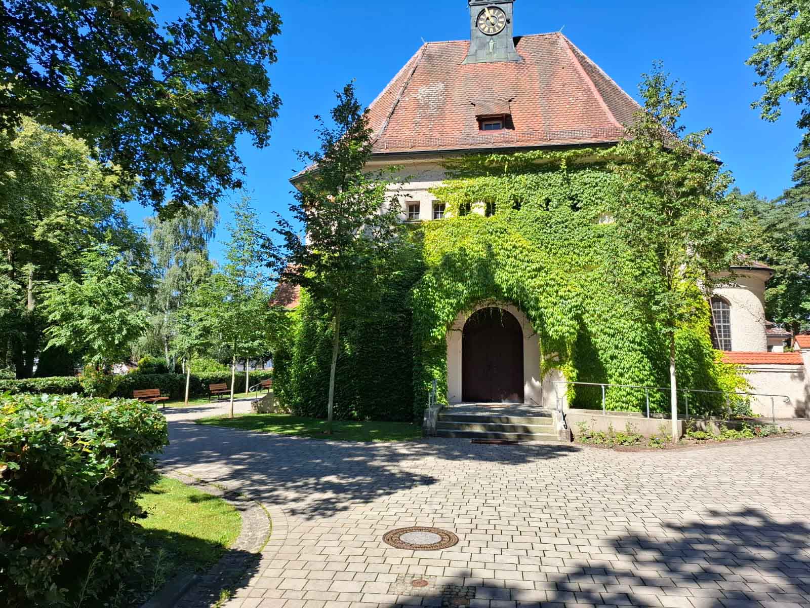 Die Kapelle des Friedhofs, ein Gebäude mit heller Mauer, ist mit grünen Pflanzen bewachsen.